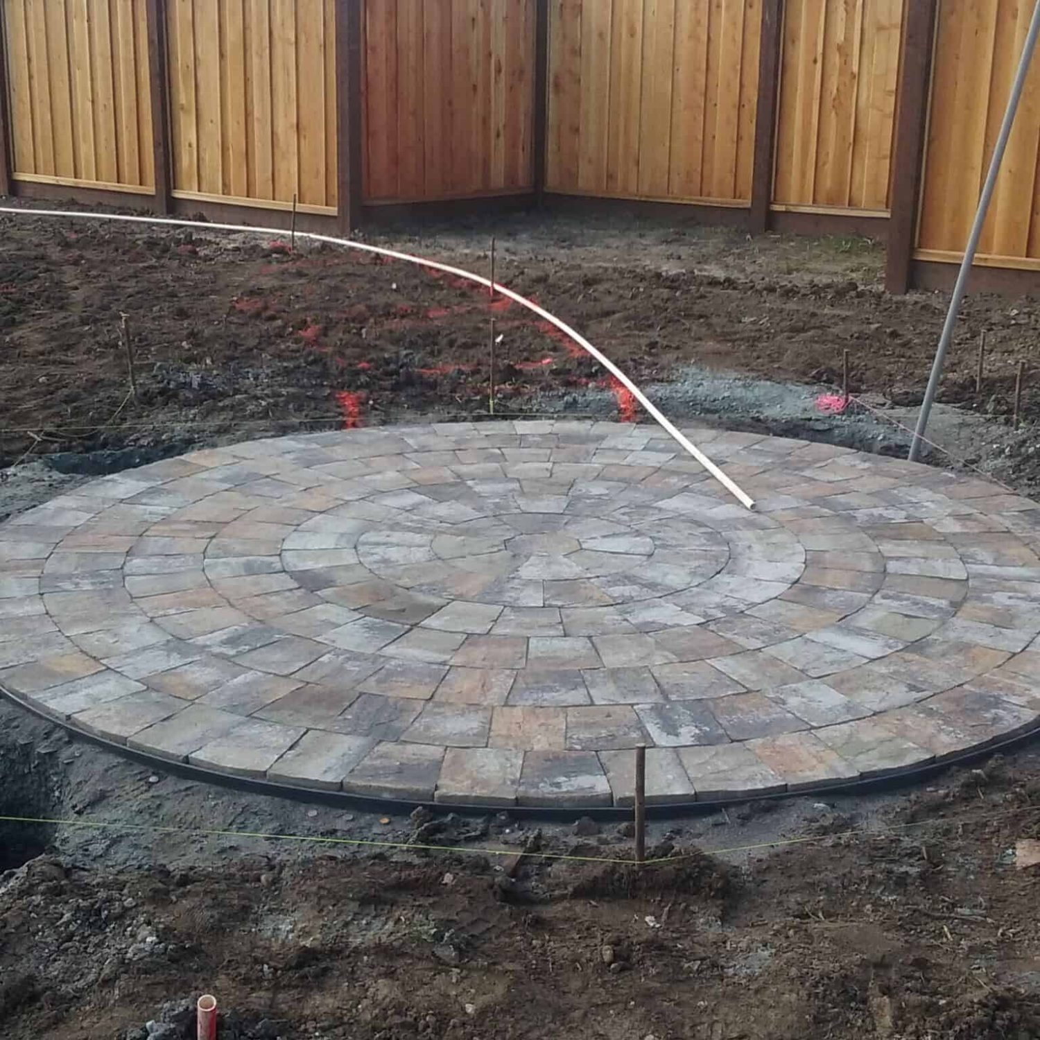 Custom outdoor paver patio in a backyard with a new wooden privacy fence and landscaped ground.