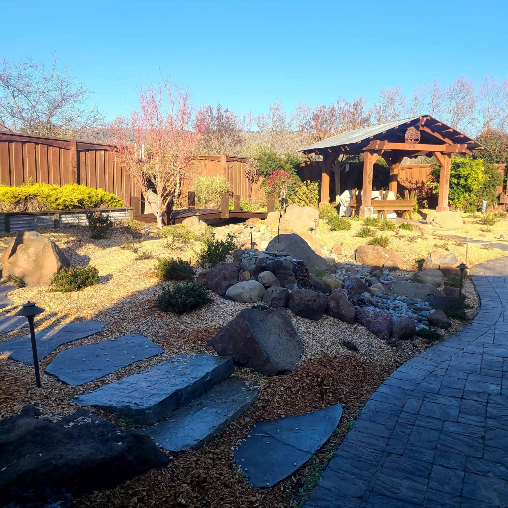 2. Beautiful backyard landscape with stone pathways, rocks, and a wooden gazebo, showcasing professional landscaping services.